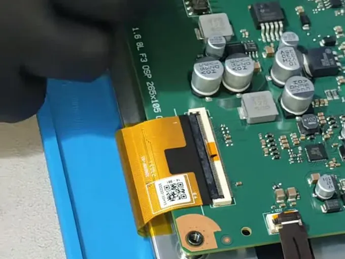 Placa eletrônica do painel com o flat cable laranja conectado, sobre o tapete de bancada